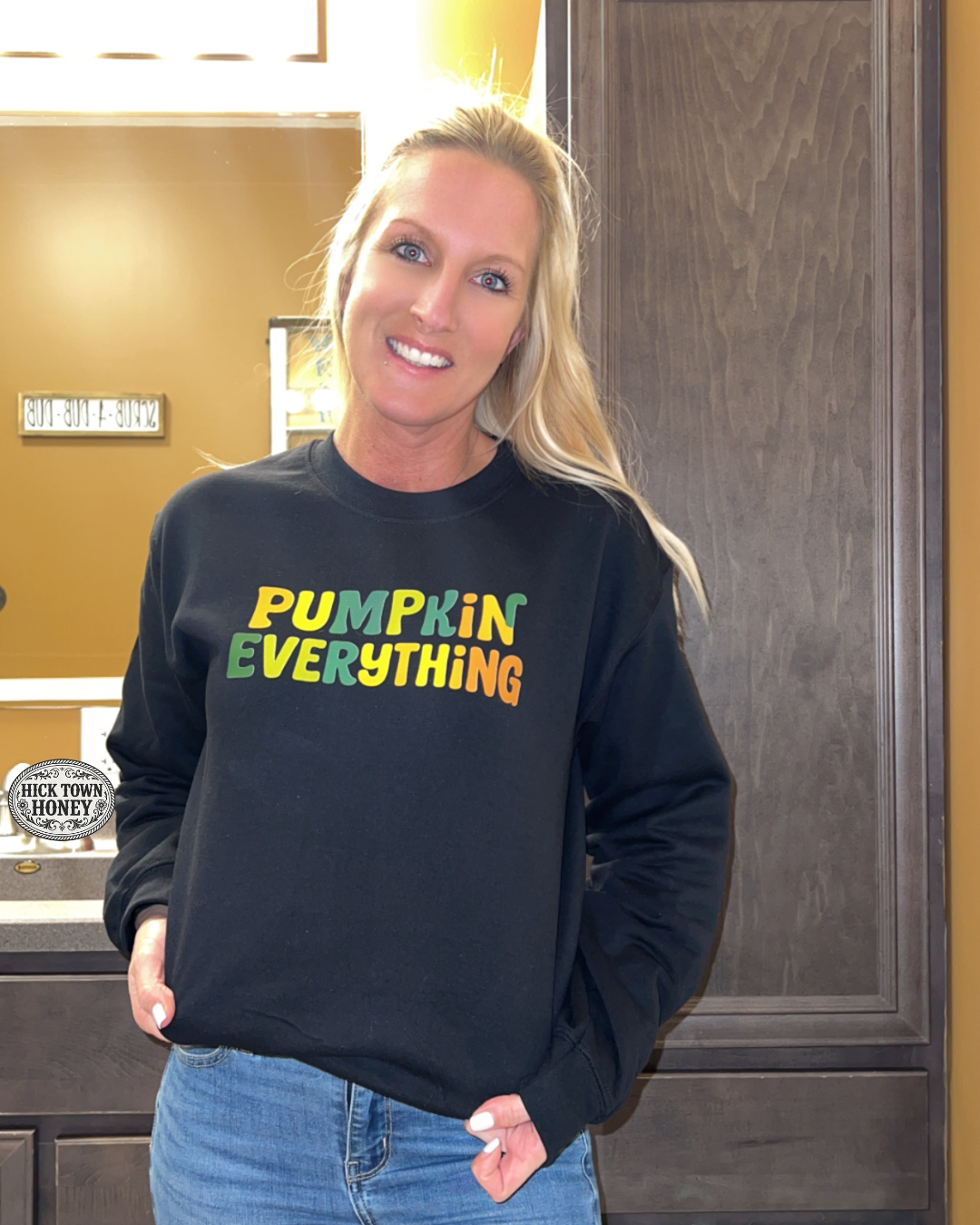 Woman wearing a black sweatshirt with colorful text standing indoors.